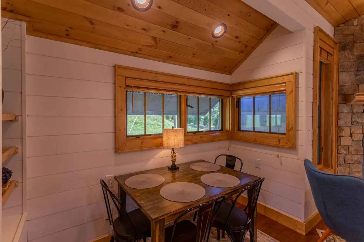 A welcoming dining area with a wooden table and black metal chairs set beside large windows that let in plenty of daylight. The setting encourages family meals, friendly conversation, and board game nights, with views that connect guests to the natural surroundings.