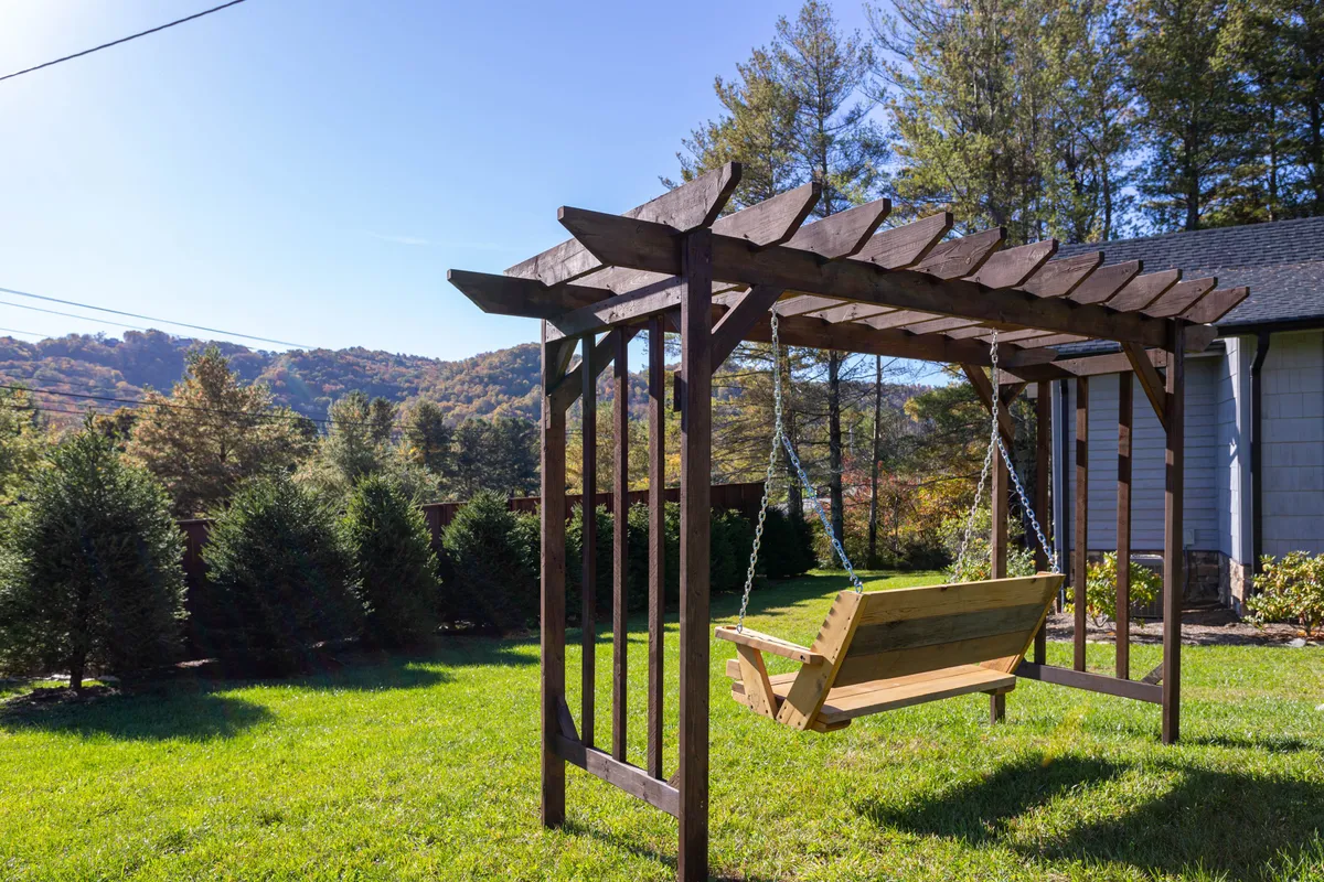 This image captures a tranquil outdoor scene featuring a custom swing suspended beneath a pergola, overlooking a sweeping mountain landscape. The natural stone and wood elements blend seamlessly with the surroundings, inviting guests to relax and enjoy the view.