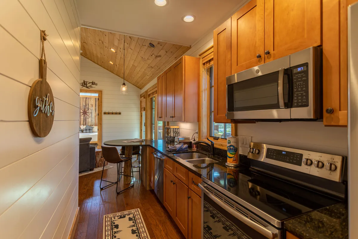 A modern, well-equipped kitchen with stainless steel appliances, ample cabinetry, bar stools, and a welcoming 'gather' sign. The setup invites shared cooking experiences and easy entertaining, perfect for families and groups returning from outdoor activities.
