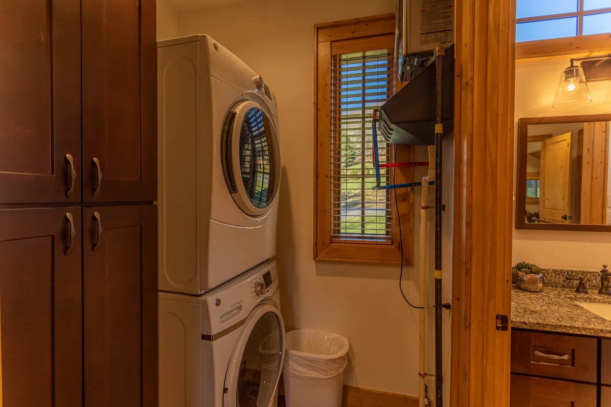 A bright, functional laundry area with a stacked washer and dryer, granite countertop, and wooden cabinetry. The practical layout assures guests of comfort and convenience for longer stays or after outdoor adventures.