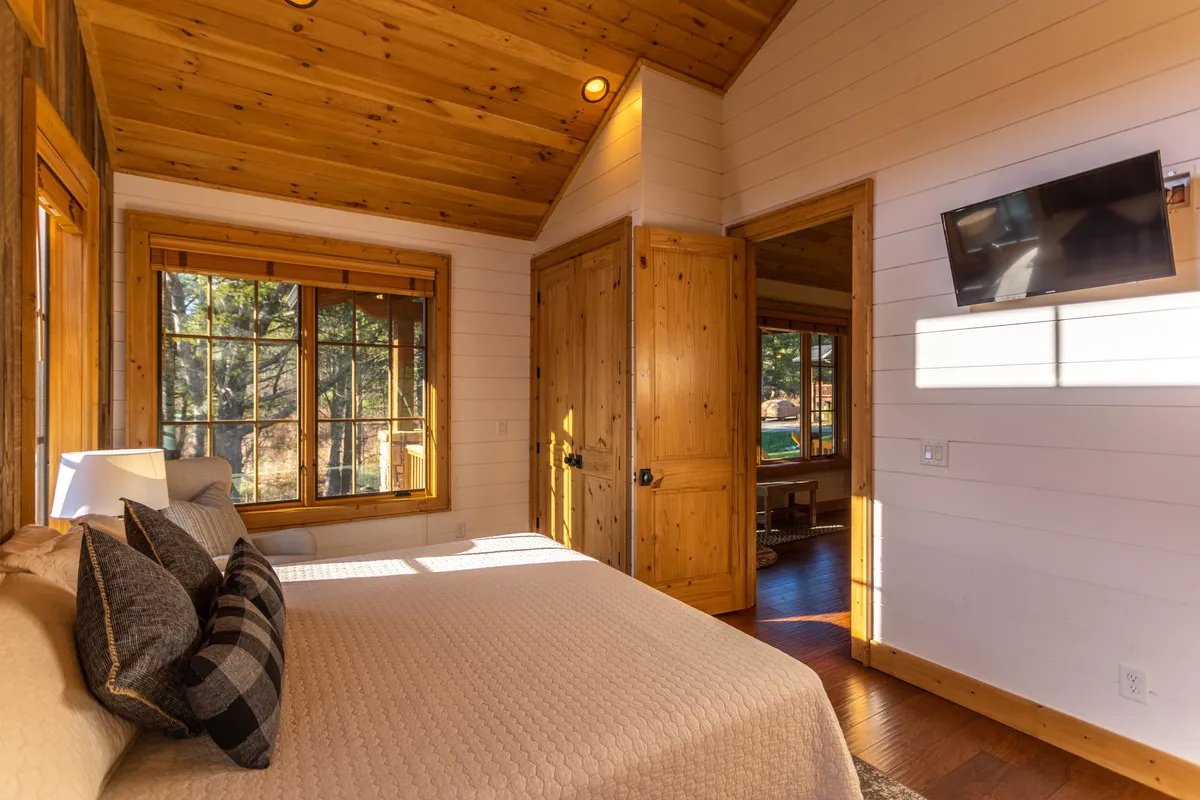 A tranquil bedroom with a plush bed, decorative pillows, and wide windows that flood the room with natural light. The windows offer peaceful views of the outdoors, reinforcing a restful connection to the mountain setting.