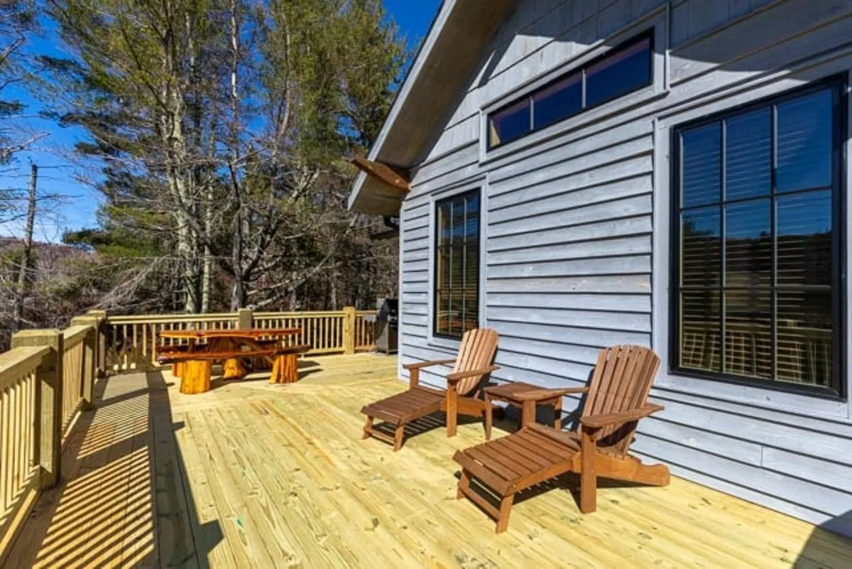 A tranquil scene of a spacious wooden deck with Adirondack chairs and a dining table, surrounded by natural wintry scenery. The deck offers panoramic views, perfect for enjoying the snowy landscape or unwinding after skiing.