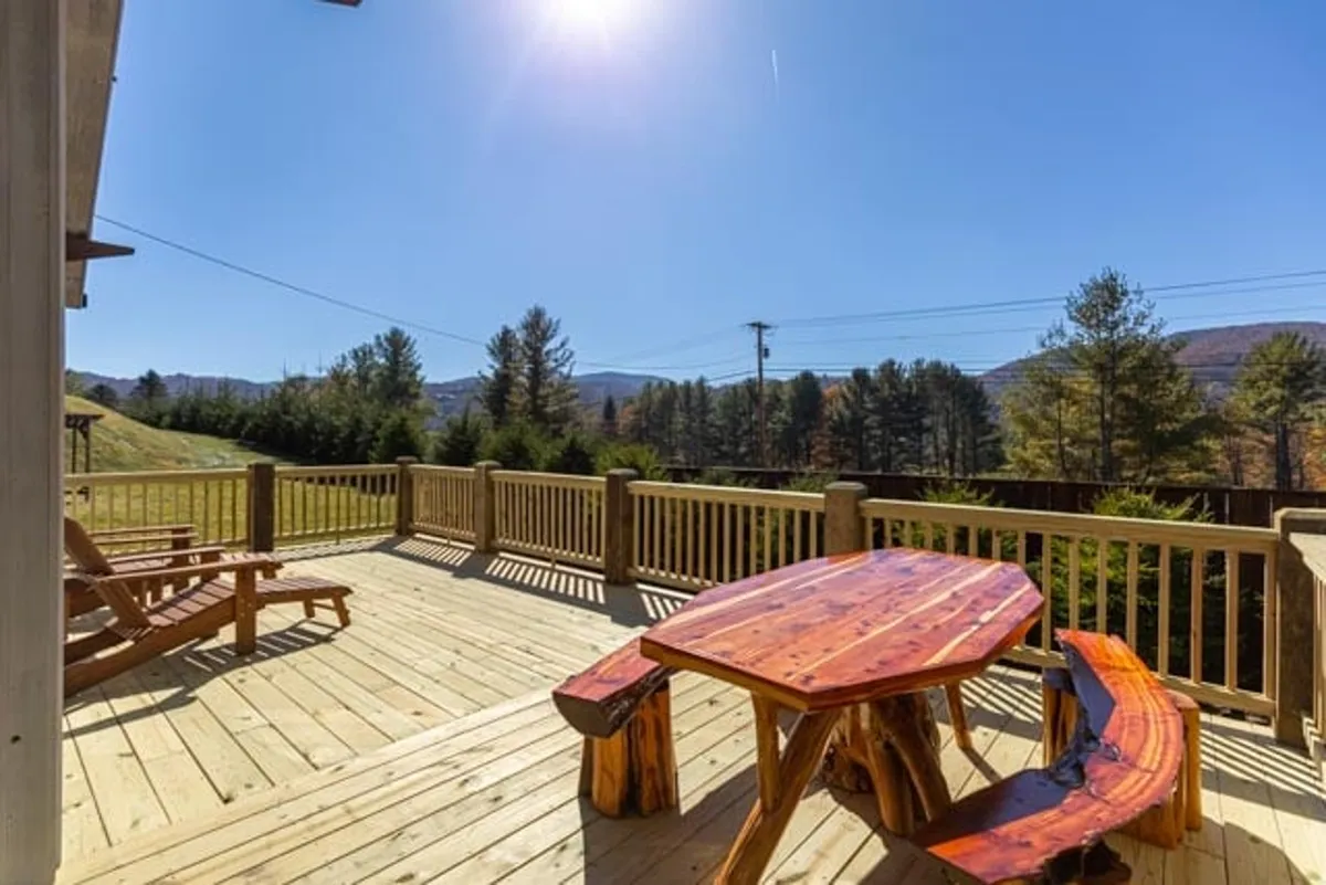 A cozy corner of the deck featuring a wooden table and an Adirondack chair, set against a natural backdrop. The setting evokes relaxation, with hints of morning coffee or evening cocoa while snow falls softly around.