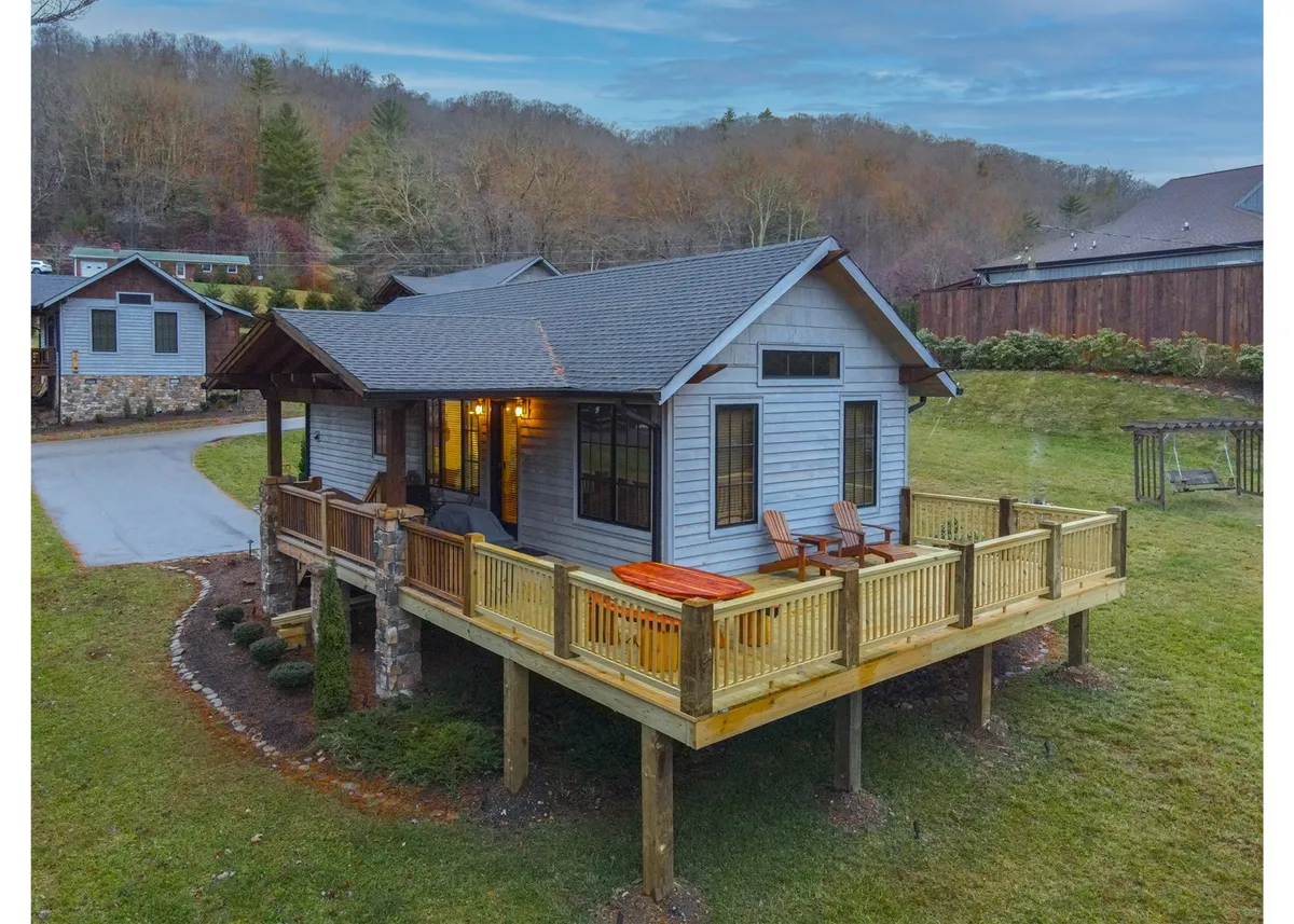 This image shows a spacious wooden deck with comfortable seating, surrounded by greenery and set against a dramatic mountain backdrop. The setting is serene, ideal for sunset watching or family gatherings outdoors.