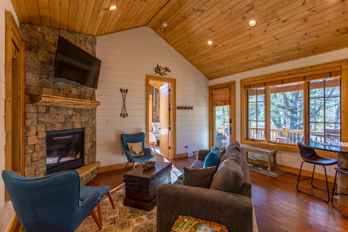 A warm and welcoming interior living area featuring a cozy fireplace, large windows with sweeping nature views, and comfortable seating arranged for relaxation or socializing. The sunset glow through the windows enhances the inviting ambiance, perfect for unwinding after outdoor adventures.